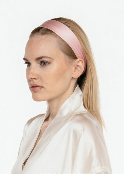 A woman in profile wearing a narrow, light pink silk headband and a matching pale pink satin top.